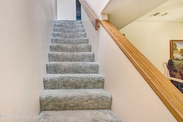 stairs with a textured ceiling and carpet flooring