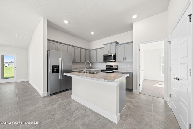 kitchen with stainless steel appliances, gray cabinets, a center island with sink, and sink