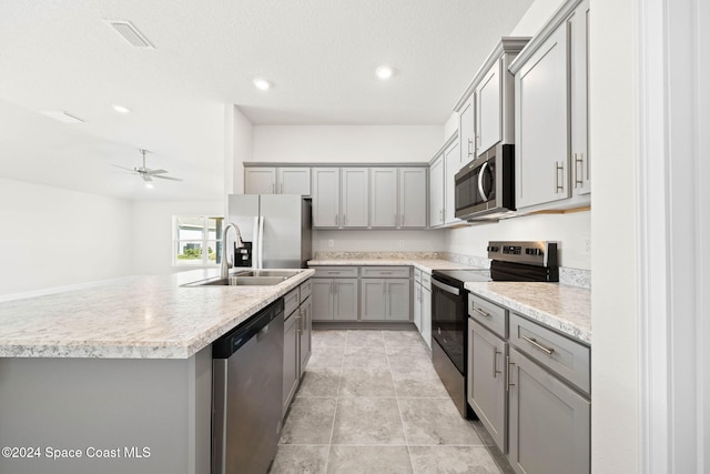 kitchen with ceiling fan, sink, gray cabinets, a center island with sink, and appliances with stainless steel finishes