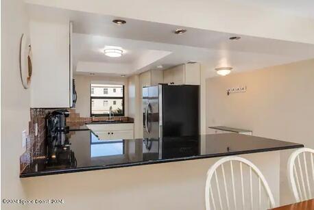 kitchen featuring stainless steel fridge, a raised ceiling, sink, and kitchen peninsula