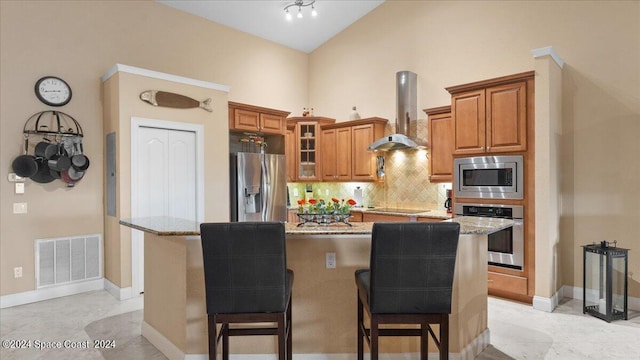 kitchen with a center island, light stone countertops, stainless steel appliances, wall chimney range hood, and a kitchen bar