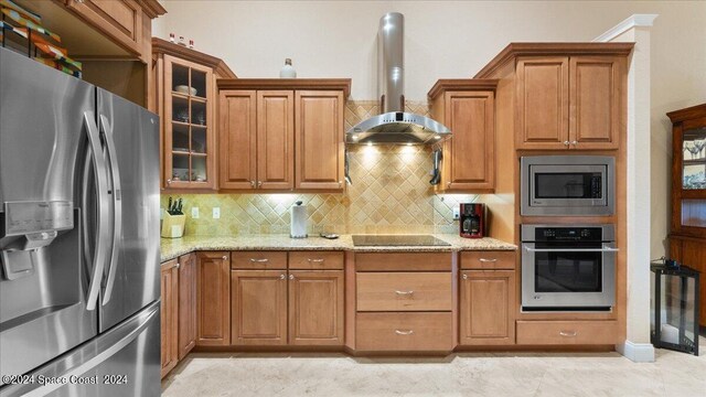 kitchen with appliances with stainless steel finishes, light stone counters, decorative backsplash, and wall chimney exhaust hood