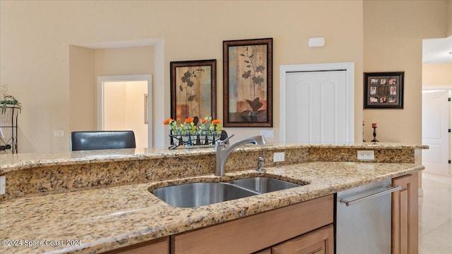 kitchen featuring stainless steel dishwasher, sink, and light stone countertops