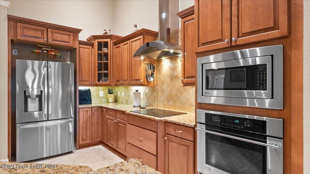 kitchen featuring tasteful backsplash, light stone counters, stainless steel appliances, and wall chimney range hood