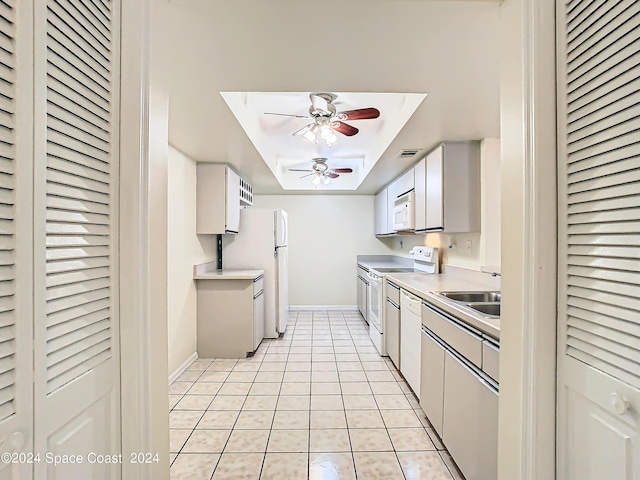 kitchen featuring white appliances, light tile patterned floors, ceiling fan, a tray ceiling, and a sink