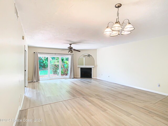 unfurnished living room with ceiling fan with notable chandelier and light hardwood / wood-style flooring