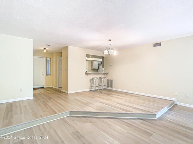 unfurnished living room with light wood-type flooring, a textured ceiling, and a notable chandelier