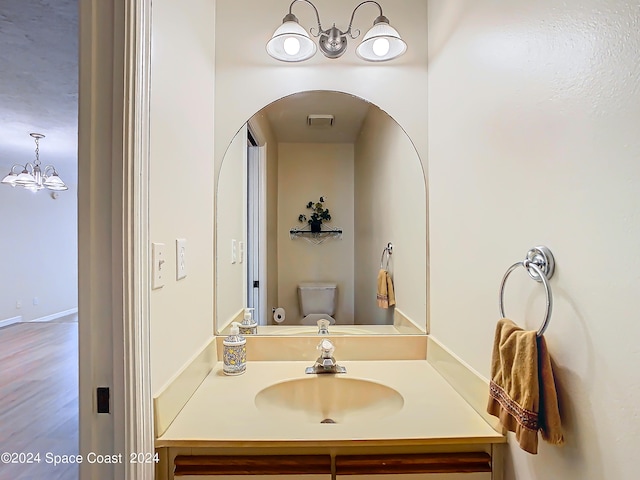 bathroom featuring wood-type flooring, toilet, a chandelier, and vanity