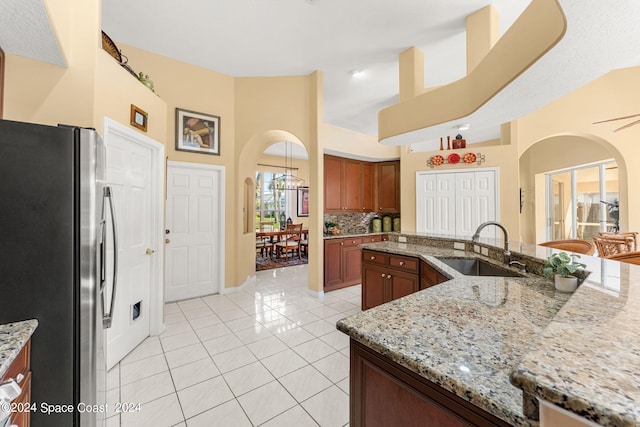 kitchen featuring light stone countertops, stainless steel refrigerator, sink, decorative backsplash, and light tile patterned flooring