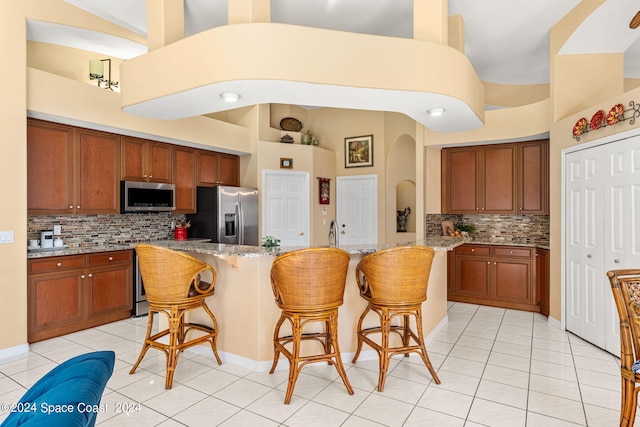 kitchen with backsplash, light tile patterned floors, appliances with stainless steel finishes, light stone counters, and a breakfast bar