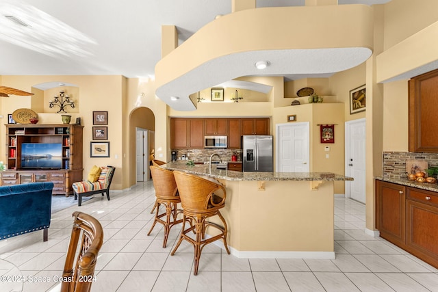 kitchen featuring backsplash, light tile patterned floors, a kitchen breakfast bar, light stone countertops, and appliances with stainless steel finishes