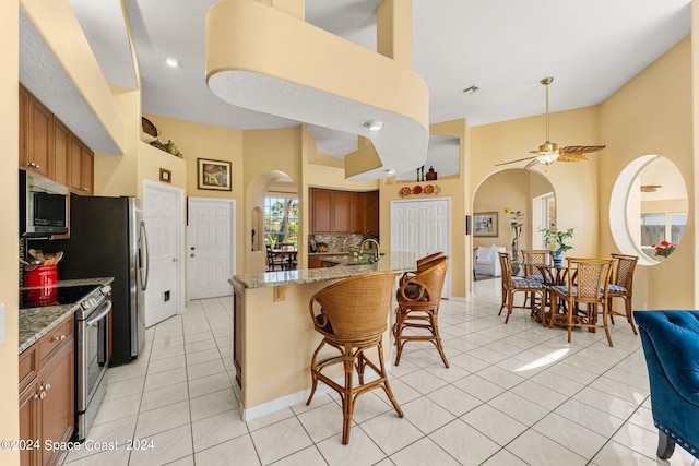 kitchen featuring light tile patterned floors, light stone countertops, stainless steel appliances, a breakfast bar area, and ceiling fan