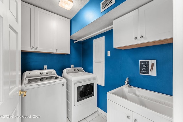 laundry area featuring light tile patterned floors, a textured ceiling, cabinets, and washer and dryer