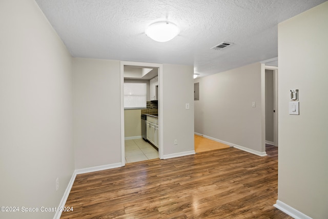 interior space with a textured ceiling, electric panel, and light hardwood / wood-style floors