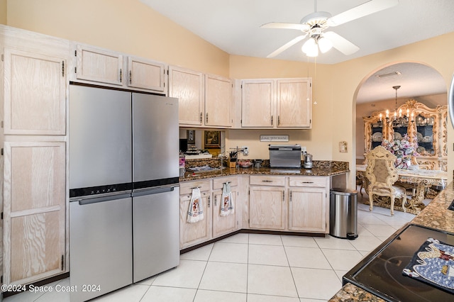 kitchen featuring ceiling fan with notable chandelier, stainless steel fridge, light brown cabinets, and dark stone counters