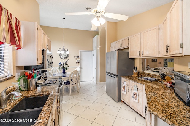 kitchen with appliances with stainless steel finishes, ceiling fan with notable chandelier, dark stone countertops, and sink