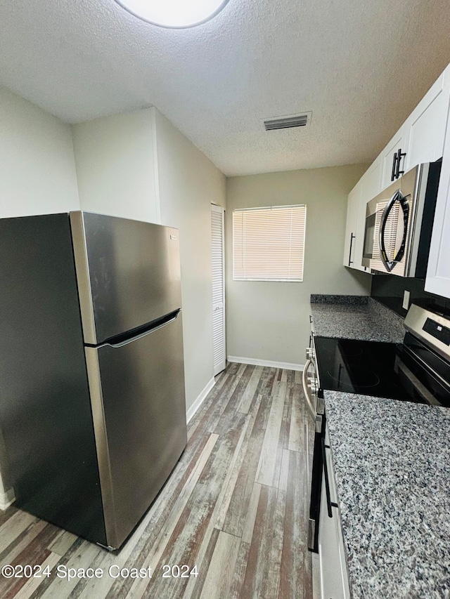 kitchen with appliances with stainless steel finishes, light hardwood / wood-style floors, white cabinetry, and a textured ceiling