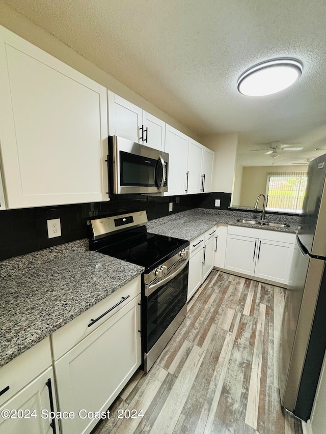 kitchen with light wood-type flooring, appliances with stainless steel finishes, sink, ceiling fan, and a textured ceiling