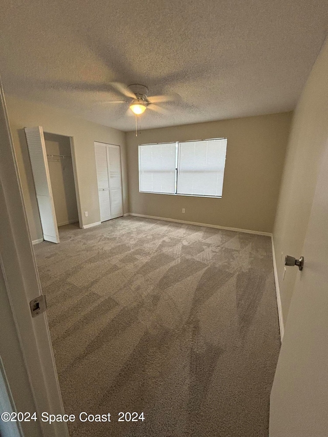 unfurnished bedroom with a textured ceiling, light colored carpet, ceiling fan, and multiple closets