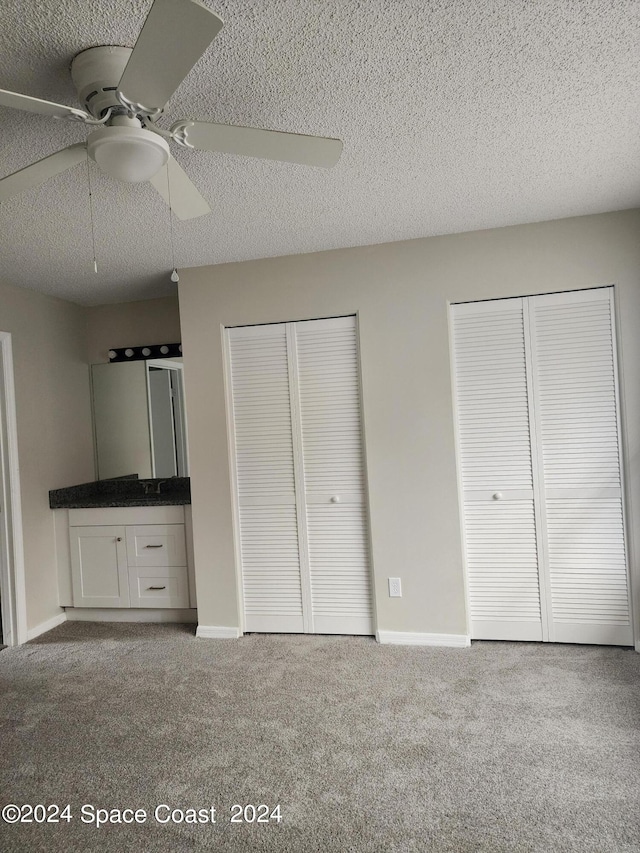 unfurnished bedroom with multiple closets, a textured ceiling, ceiling fan, and carpet