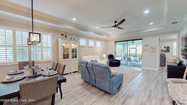 living room featuring light hardwood / wood-style flooring, ornamental molding, ceiling fan with notable chandelier, and a tray ceiling