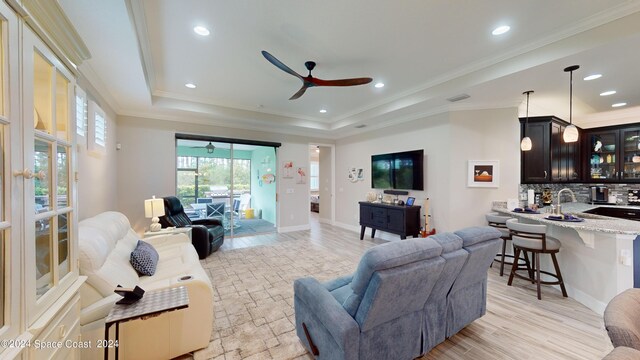 living room featuring a raised ceiling, light hardwood / wood-style flooring, ornamental molding, sink, and ceiling fan