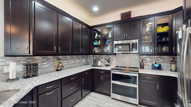 kitchen with light hardwood / wood-style flooring, stainless steel appliances, light stone counters, and decorative backsplash