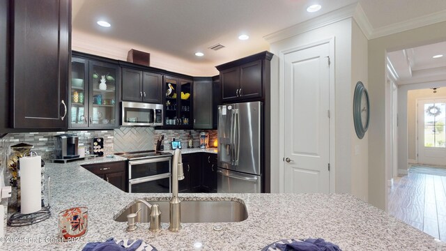 kitchen featuring crown molding, stainless steel appliances, wood-type flooring, light stone counters, and decorative backsplash