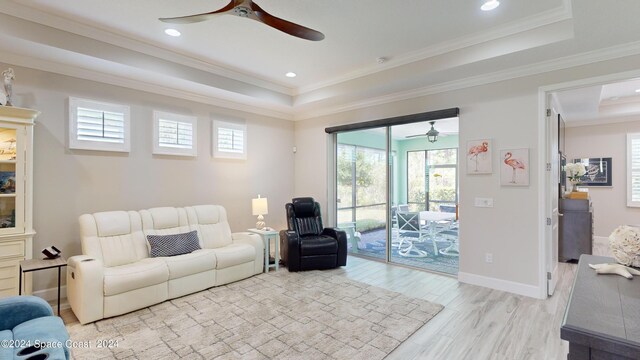 living room featuring ceiling fan, a raised ceiling, crown molding, and light hardwood / wood-style flooring