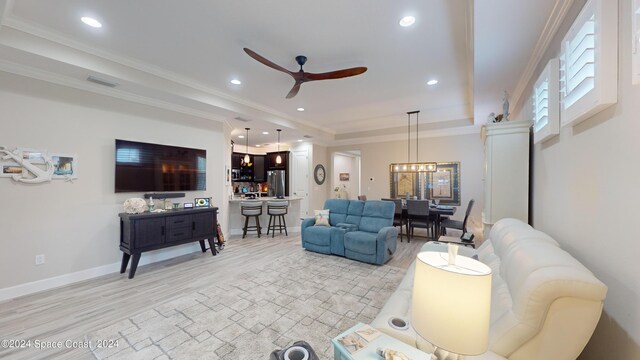 living room featuring ceiling fan with notable chandelier, ornamental molding, a tray ceiling, and light hardwood / wood-style floors