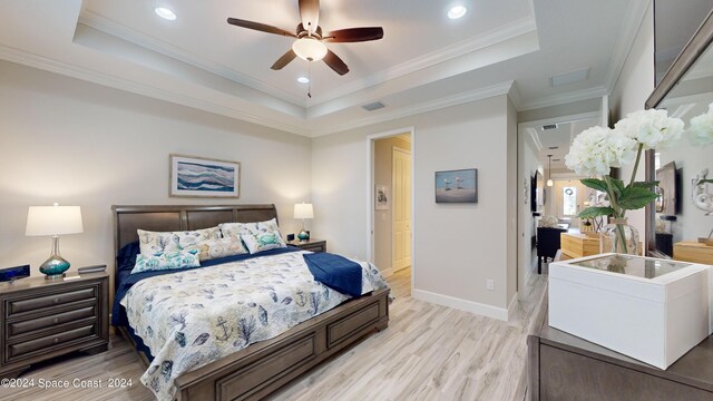 bedroom with light wood-type flooring, ceiling fan, a raised ceiling, and ornamental molding