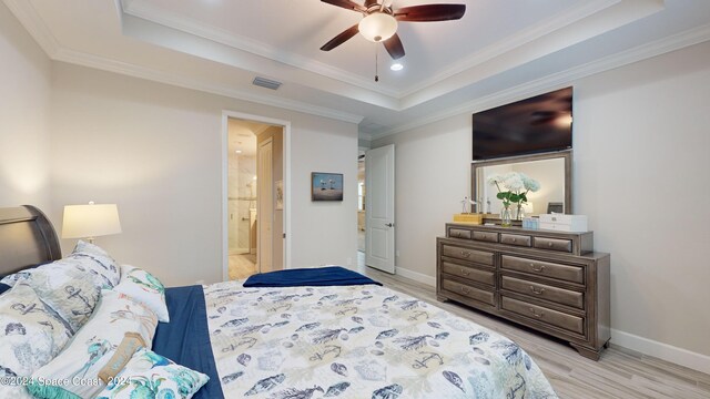 bedroom featuring a raised ceiling, ensuite bath, ornamental molding, and ceiling fan