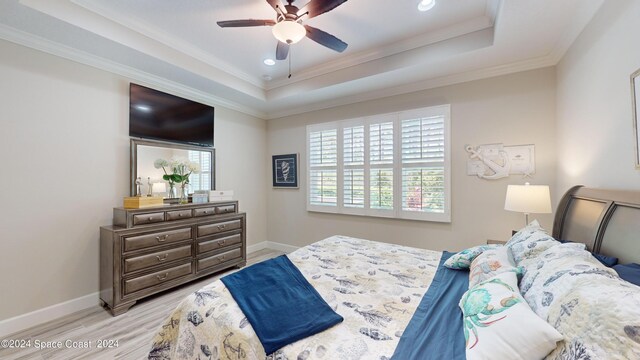 bedroom featuring ceiling fan, a raised ceiling, light hardwood / wood-style floors, and ornamental molding