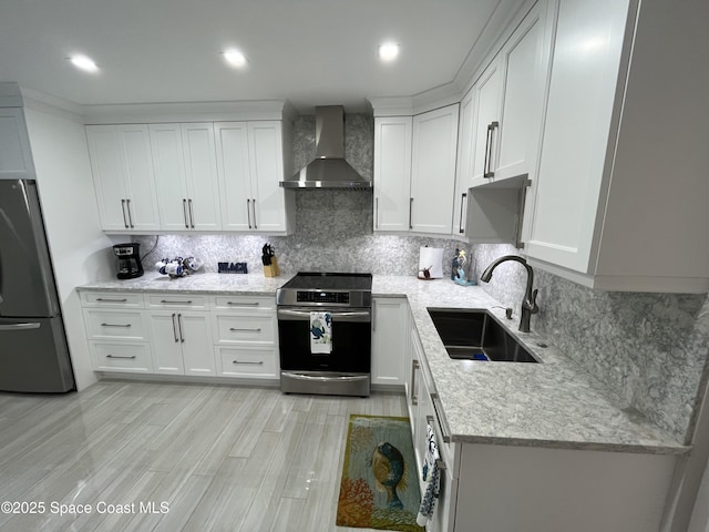 kitchen with wall chimney exhaust hood, sink, tasteful backsplash, appliances with stainless steel finishes, and white cabinets