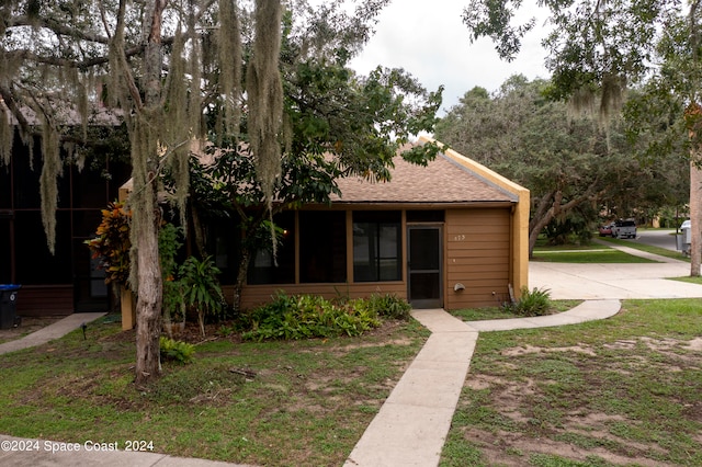 view of front of home with a shingled roof, a front yard, and a sunroom