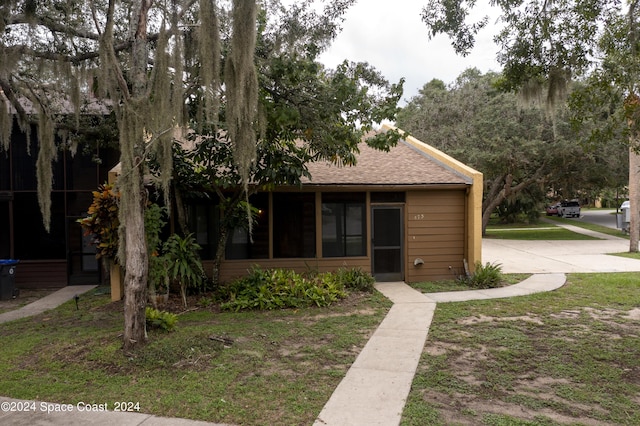 view of front of house featuring a front yard, a sunroom, driveway, and a shingled roof