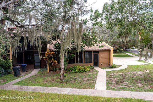 view of property hidden behind natural elements with a front lawn and a sunroom