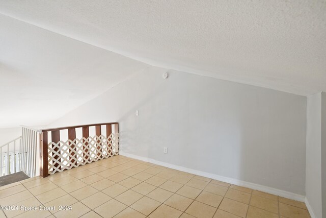 bonus room featuring lofted ceiling, light tile patterned floors, and a textured ceiling