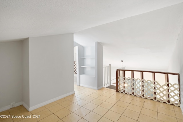 unfurnished room with light tile patterned flooring, a textured ceiling, baseboards, built in shelves, and lofted ceiling