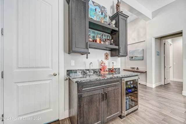 bar featuring light wood-type flooring, a textured ceiling, sink, beverage cooler, and dark stone countertops