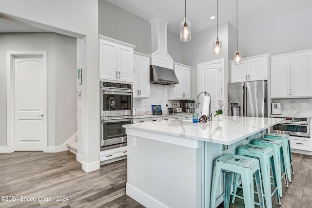 kitchen with white cabinets, appliances with stainless steel finishes, a kitchen island with sink, and pendant lighting