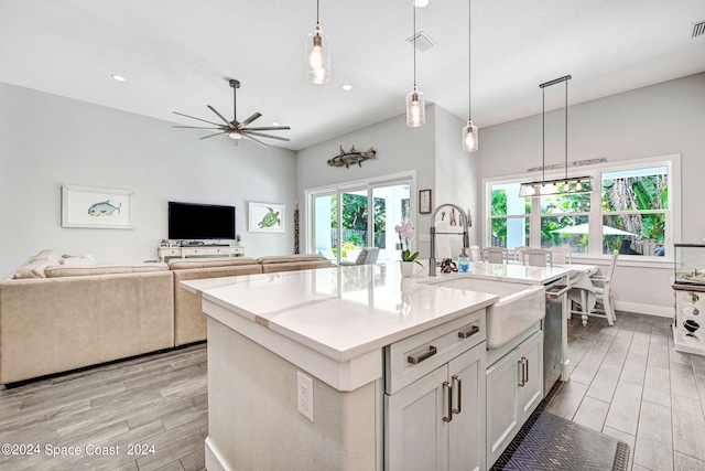 kitchen featuring hanging light fixtures, white cabinetry, ceiling fan, light hardwood / wood-style flooring, and a center island with sink