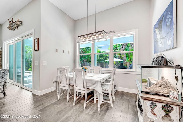 dining room featuring a notable chandelier, a wealth of natural light, wood-type flooring, and high vaulted ceiling