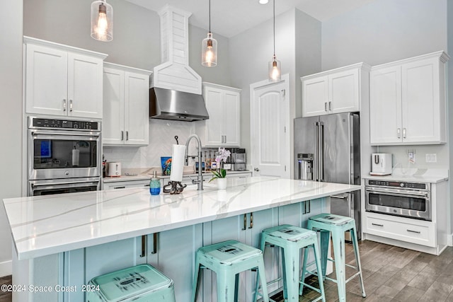 kitchen featuring pendant lighting, an island with sink, a kitchen bar, and white cabinetry