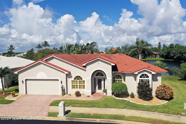 mediterranean / spanish home featuring a garage, a water view, and a front lawn