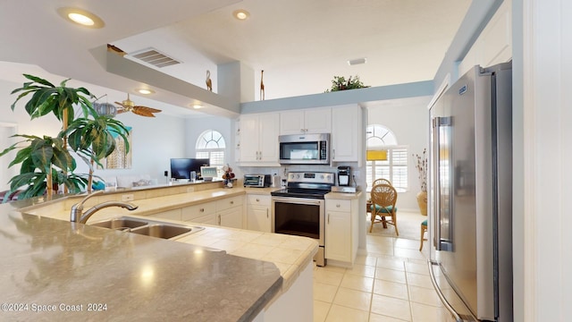 kitchen with light tile patterned floors, appliances with stainless steel finishes, kitchen peninsula, sink, and white cabinetry