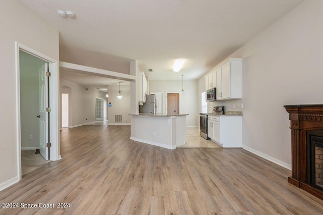 kitchen featuring white cabinets, light wood-type flooring, a textured ceiling, appliances with stainless steel finishes, and light stone counters