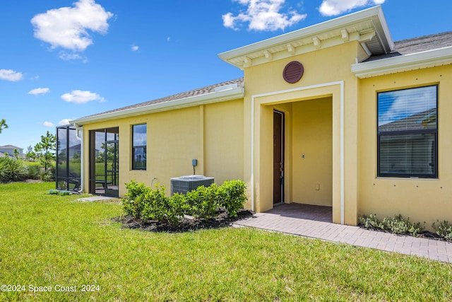 view of exterior entry featuring central AC, a lawn, and stucco siding