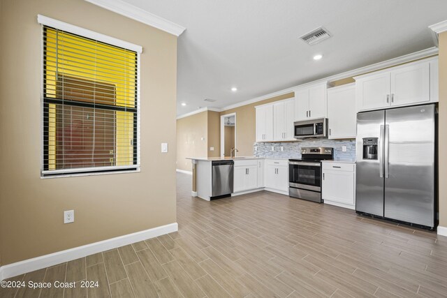 kitchen featuring light wood-type flooring, ornamental molding, tasteful backsplash, stainless steel appliances, and white cabinets