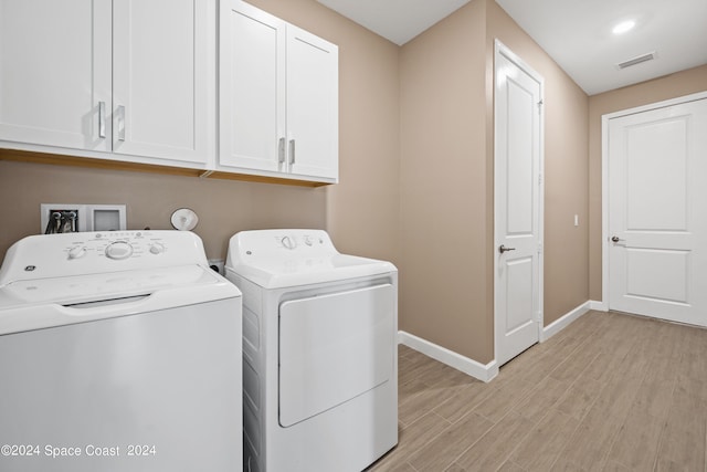 clothes washing area featuring washing machine and dryer, visible vents, baseboards, cabinet space, and light wood finished floors